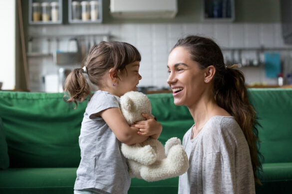 Smiling young loving mum talking with little preschool daughter with favorite stuffed toy, playing in living room at home, mother laughing with child, babysitter playing with pupil
